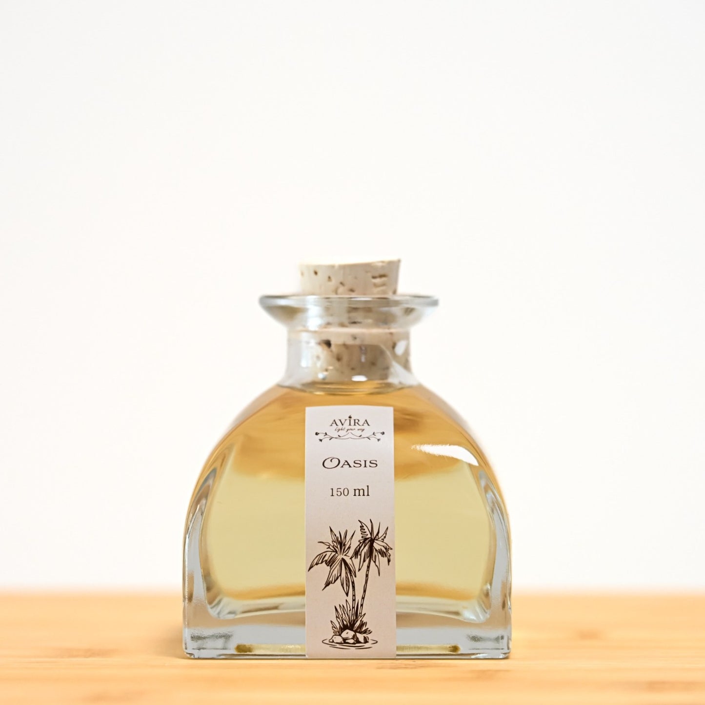 מפיץ ריח 150 מ"ל בניחוח אואזיס, בכלי זכוכית יפהפה בצורת פירמידה עם פאות מקומרות אטום בפקק שעם – ועליו איור שחור של דקלים בנווה מדבר.