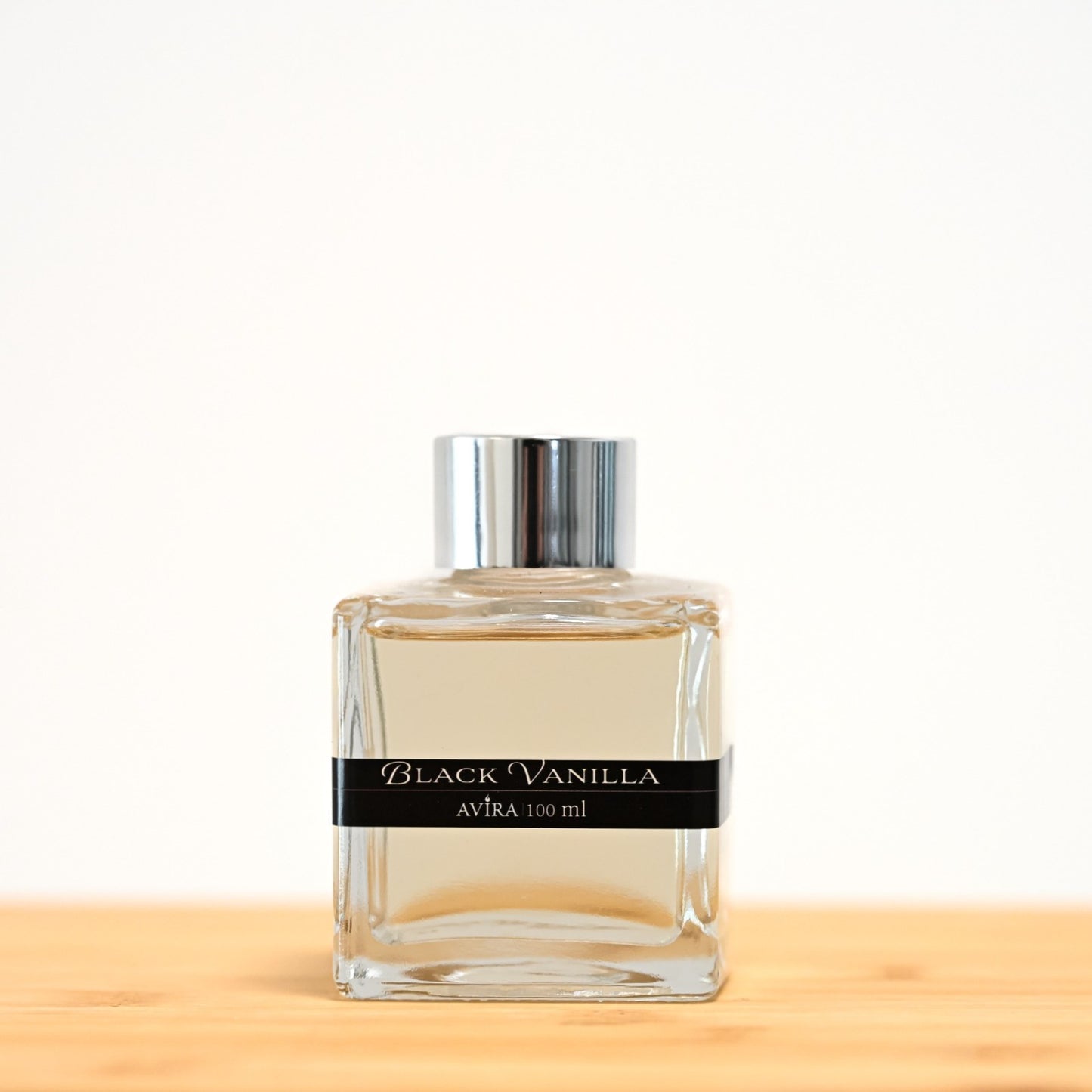 מפיץ ריח 100 מ"ל בניחוח בלאק ונילה, בכלי זכוכית שקוף בצורת קובייה – אטום בפקק ומלווה בקולר כסוף – ובחזית מדבקת פס שחורה.