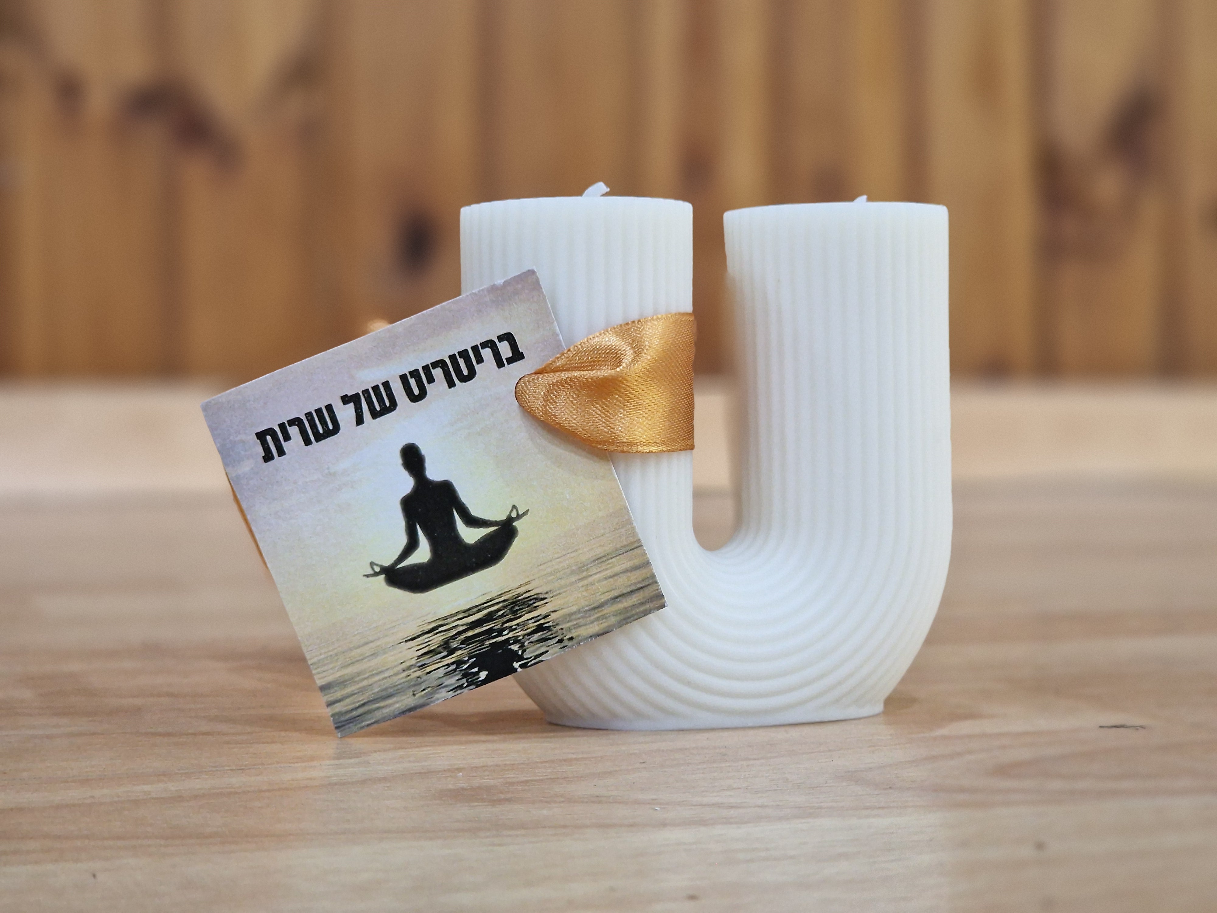 נר לבן דקורטיבי מעוצב בצורת האות יו באנגלית, עם שני פתילים, ועליו נכרך סרט עם פתק והכיתוב "בריטריט של שרית"