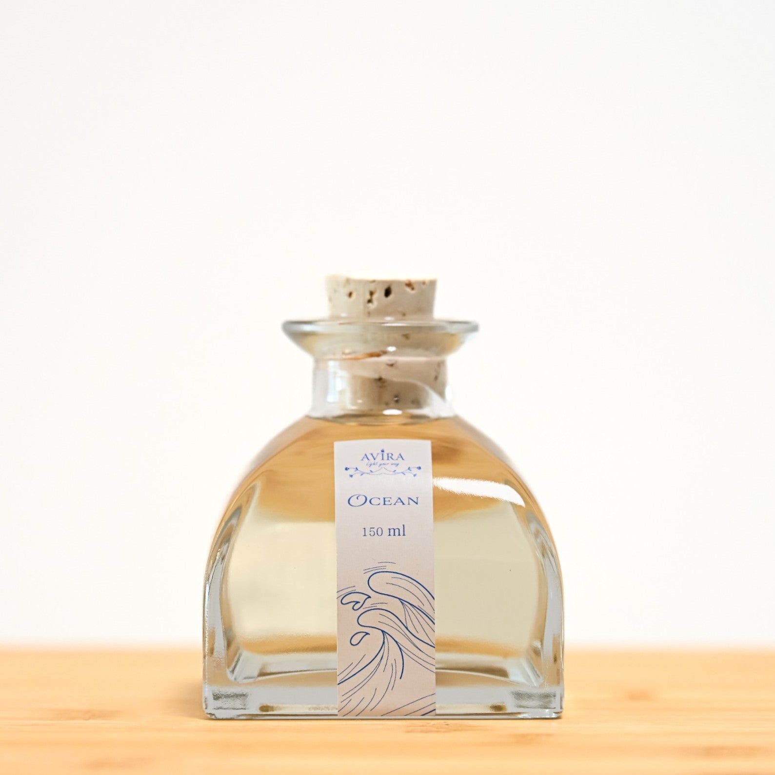 מפיץ ריח 150 מ"ל בניחוח אושן, בכלי זכוכית יפהפה בצורת פירמידה עם פאות מקומרות אטום בפקק שעם – ועליו איור כחול של גלי אוקיינוס.