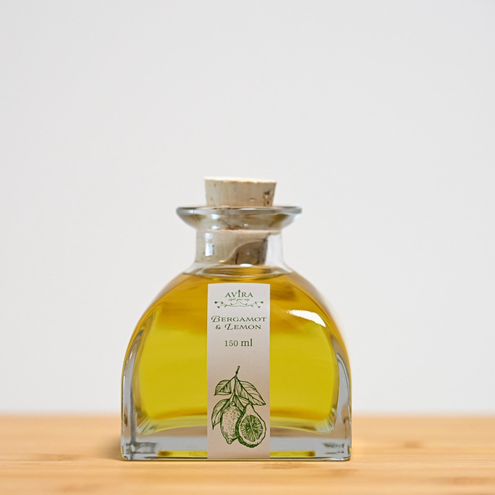 מפיץ ריח 150 מ"ל בניחוח ברגמוט ולימון, בכלי זכוכית יפהפה בצורת פירמידה עם פאות מקומרות אטום בפקק שעם – ועליו איור ירקרק של הדרים.