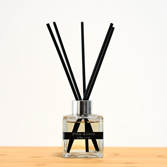 מפיץ ריח 100 מ"ל בניחוח לוטוס ורוד עם מקלות שחורים, בכלי זכוכית שקוף בצורת קובייה – אטום בפקק ומלווה בקולר כסוף – ובחזית מדבקת פס שחורה.