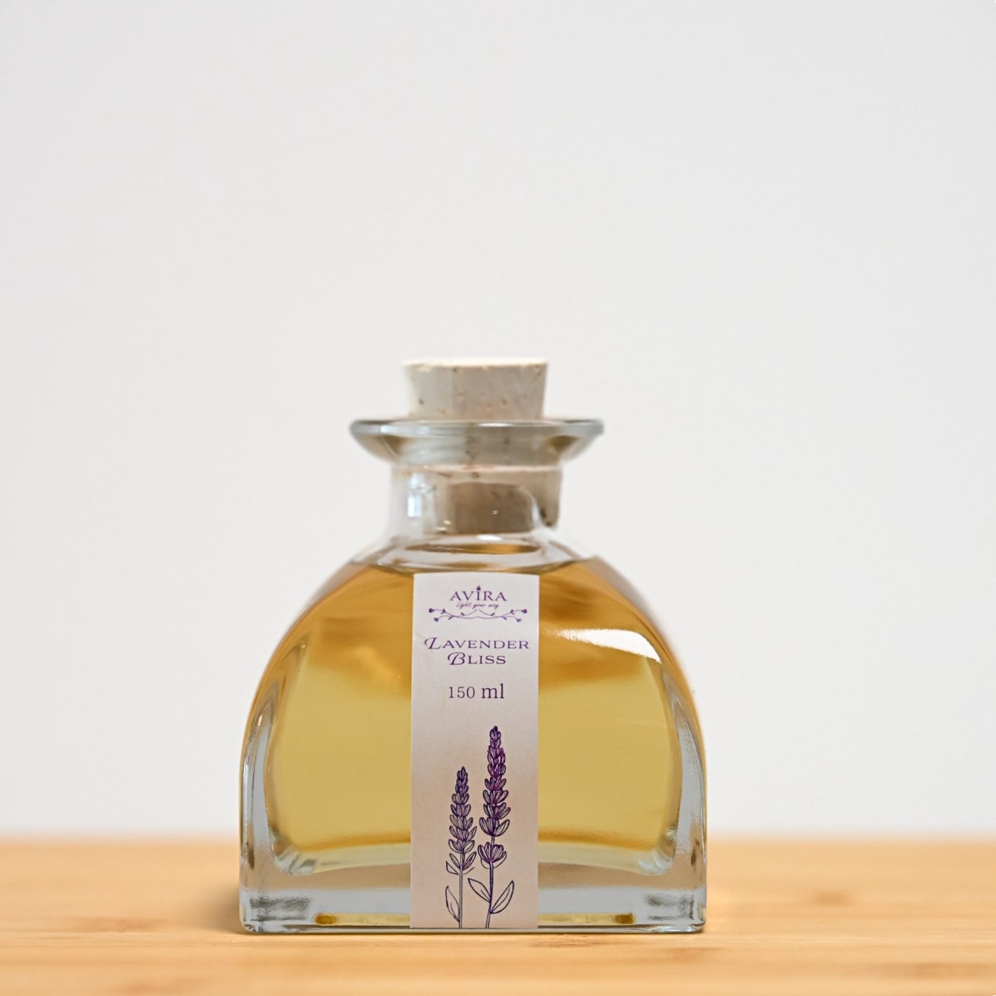 מפיץ ריח 150 מ"ל בניחוח לבנדר מפנק, בכלי זכוכית יפהפה בצורת פירמידה עם פאות מקומרות אטום בפקק שעם – ועליו איור סגלגל של צמחי לבנדר.