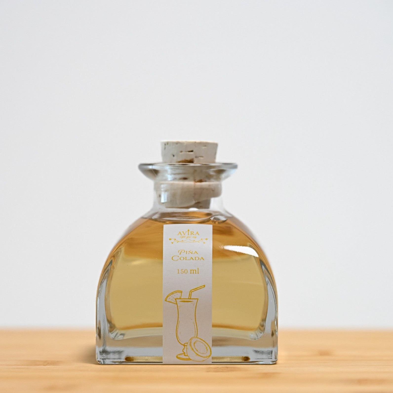 מפיץ ריח 150 מ"ל בניחוח פינה קולדה, בכלי זכוכית יפהפה בצורת פירמידה עם פאות מקומרות אטום בפקק שעם – ועליו איור כתום של קוקטייל.