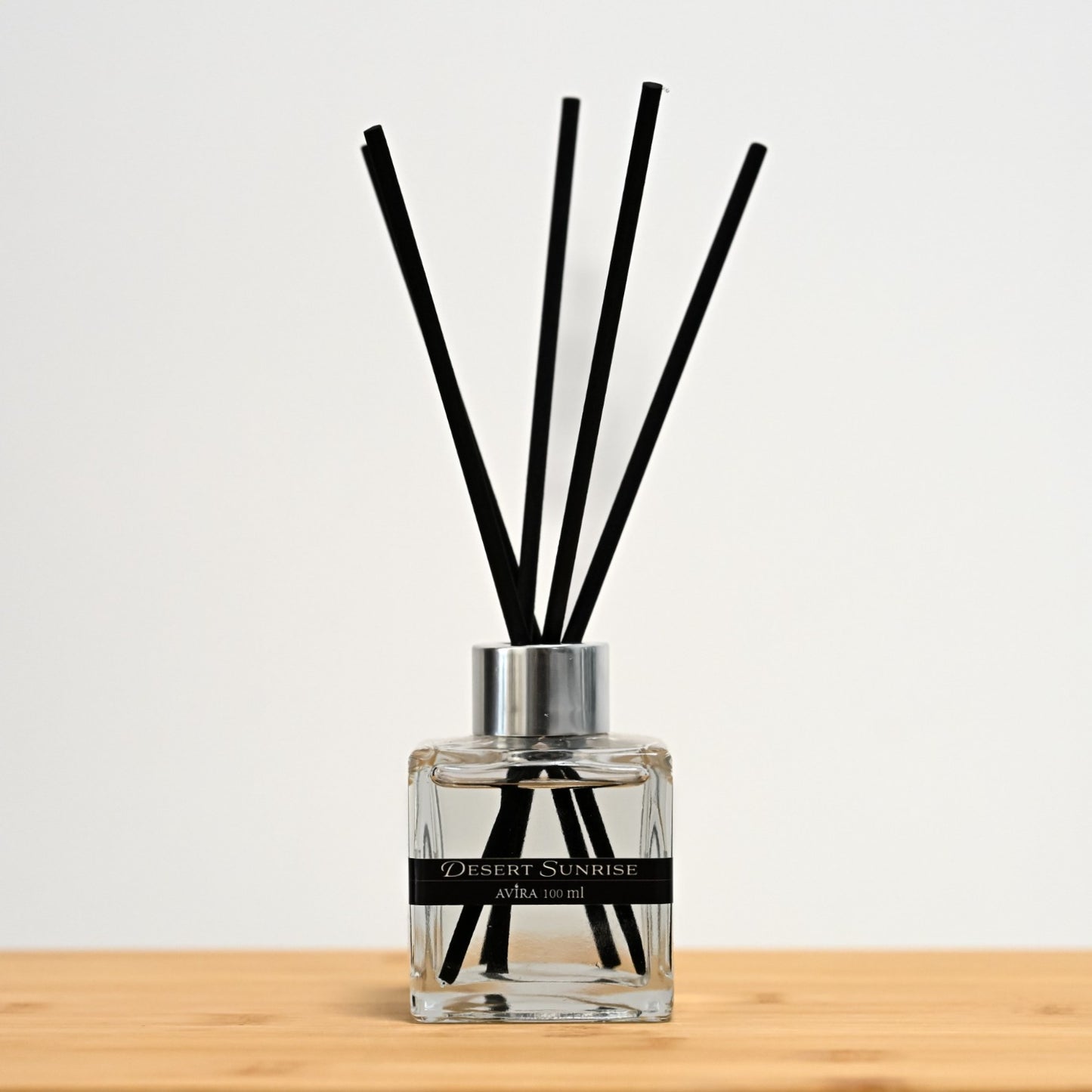 מפיץ ריח 100 מ"ל בניחוח זריחה במדבר עם מקלות שחורים, בכלי זכוכית שקוף בצורת קובייה – אטום בפקק ומלווה בקולר כסוף – ובחזית מדבקת פס שחורה.