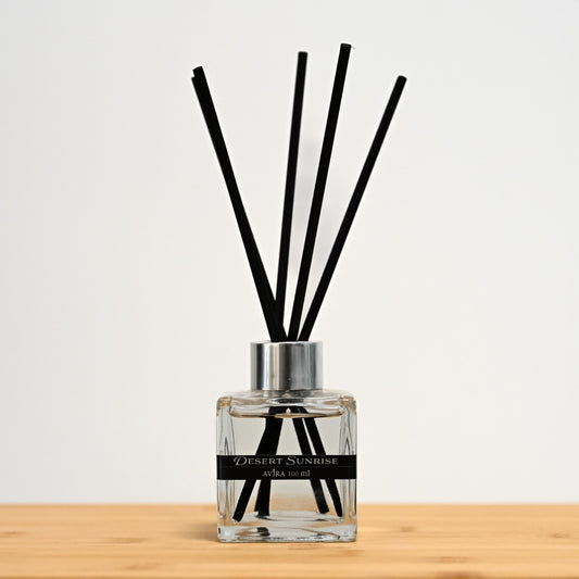 מפיץ ריח 100 מ"ל בניחוח זריחה במדבר עם מקלות שחורים, בכלי זכוכית שקוף בצורת קובייה – אטום בפקק ומלווה בקולר כסוף – ובחזית מדבקת פס שחורה.