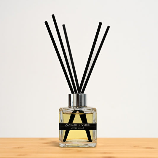 מפיץ ריח 100 מ"ל בניחוח פריחת היסמין עם מקלות שחורים, בכלי זכוכית שקוף בצורת קובייה – אטום בפקק ומלווה בקולר כסוף – ובחזית מדבקת פס שחורה.