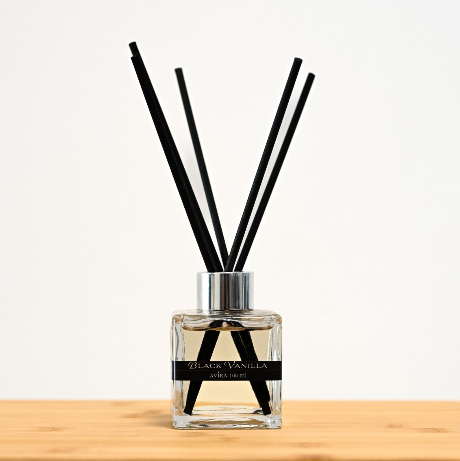 מפיץ ריח 100 מ"ל בניחוח בלאק ונילה עם מקלות שחורים, בכלי זכוכית שקוף בצורת קובייה – אטום בפקק ומלווה בקולר כסוף – ובחזית מדבקת פס שחורה.