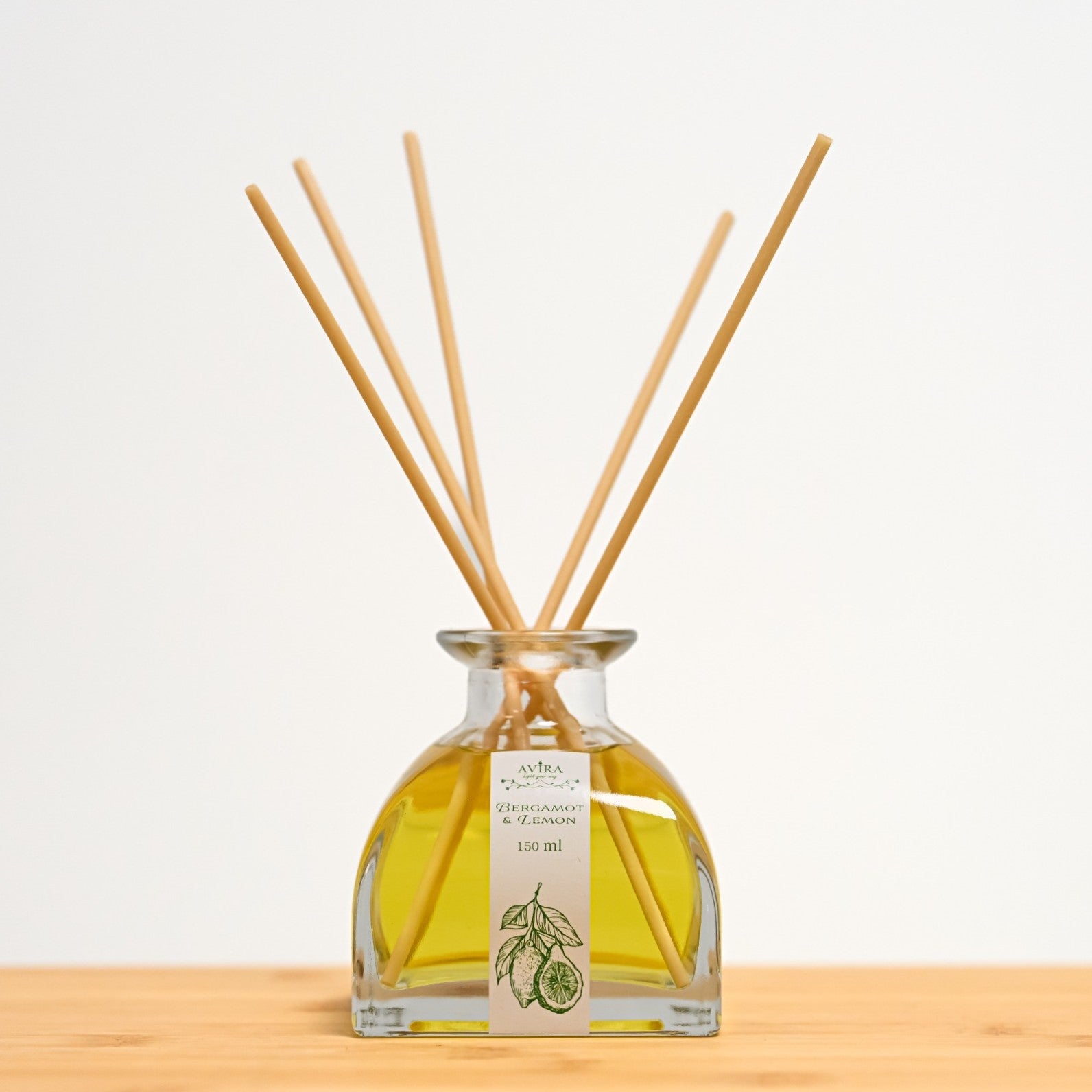 מפיץ ריח 150 מ"ל בניחוח ברגמוט ולימון עם מקלות דמויי עץ, בכלי זכוכית יפהפה בצורת פירמידה עם פאות מקומרות אטום בפקק שעם – ועליו איור ירקרק של הדרים.