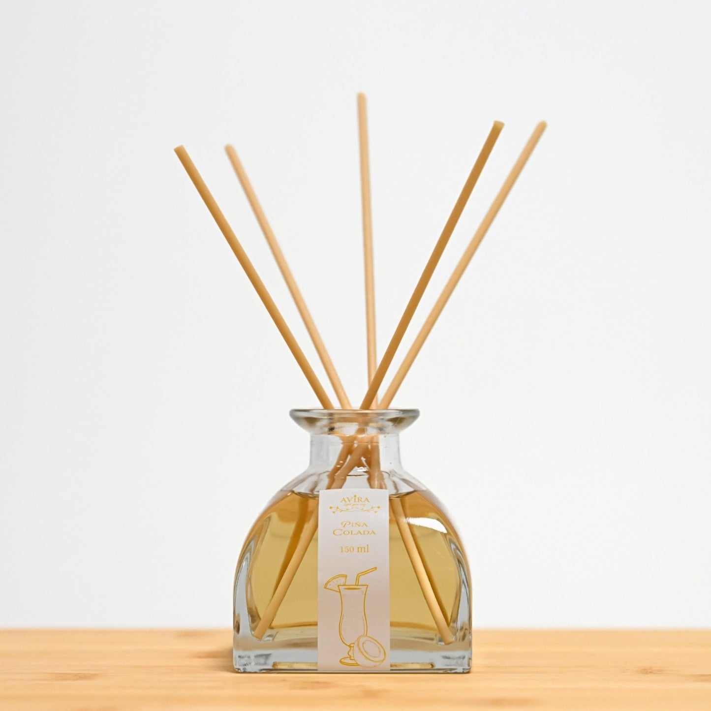 מפיץ ריח 150 מ"ל בניחוח פינה קולדה עם מקלות דמויי עץ, בכלי זכוכית יפהפה בצורת פירמידה עם פאות מקומרות אטום בפקק שעם – ועליו איור כתום של קוקטייל.