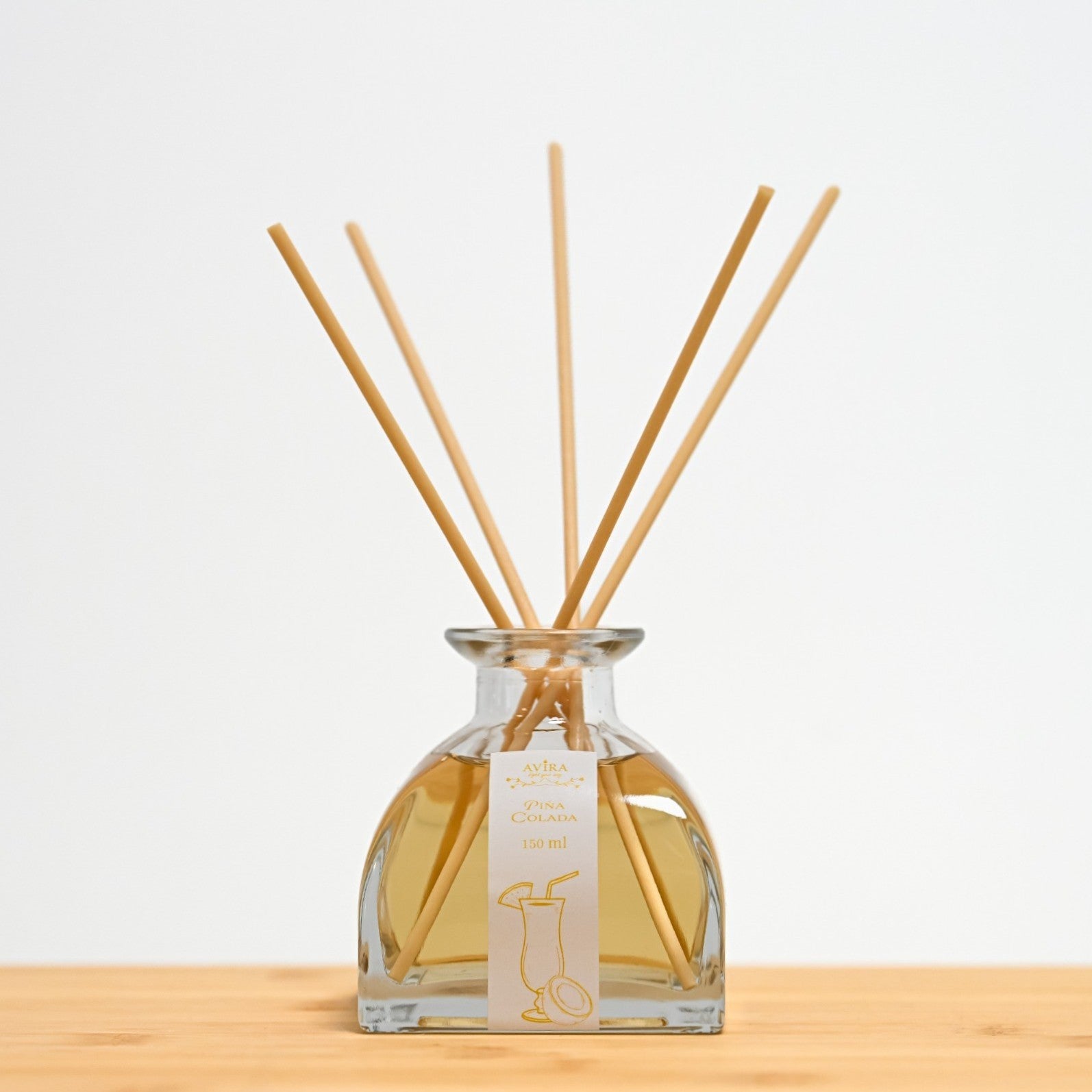 מפיץ ריח 150 מ"ל בניחוח פינה קולדה עם מקלות דמויי עץ, בכלי זכוכית יפהפה בצורת פירמידה עם פאות מקומרות אטום בפקק שעם – ועליו איור כתום של קוקטייל.