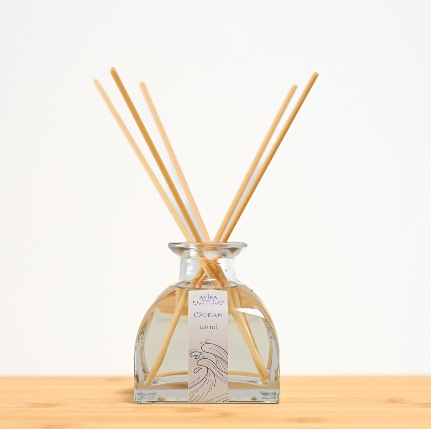 מפיץ ריח 150 מ"ל בניחוח אושן עם מקלות דמויי עץ, בכלי זכוכית יפהפה בצורת פירמידה עם פאות מקומרות אטום בפקק שעם – ועליו איור כחול של גלי אוקיינוס.