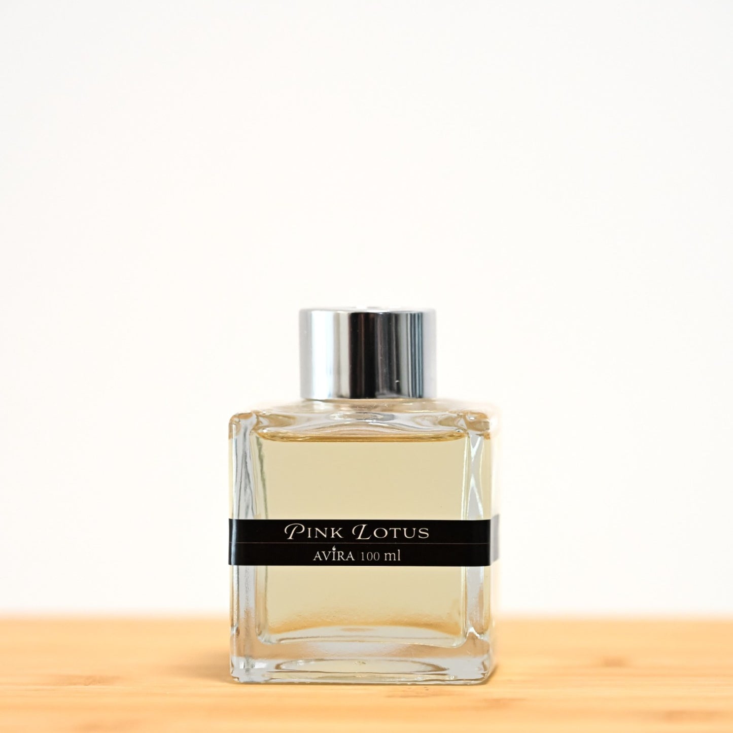 מפיץ ריח 100 מ"ל בניחוח לוטוס ורוד, בכלי זכוכית שקוף בצורת קובייה – אטום בפקק ומלווה בקולר כסוף – ובחזית מדבקת פס שחורה.