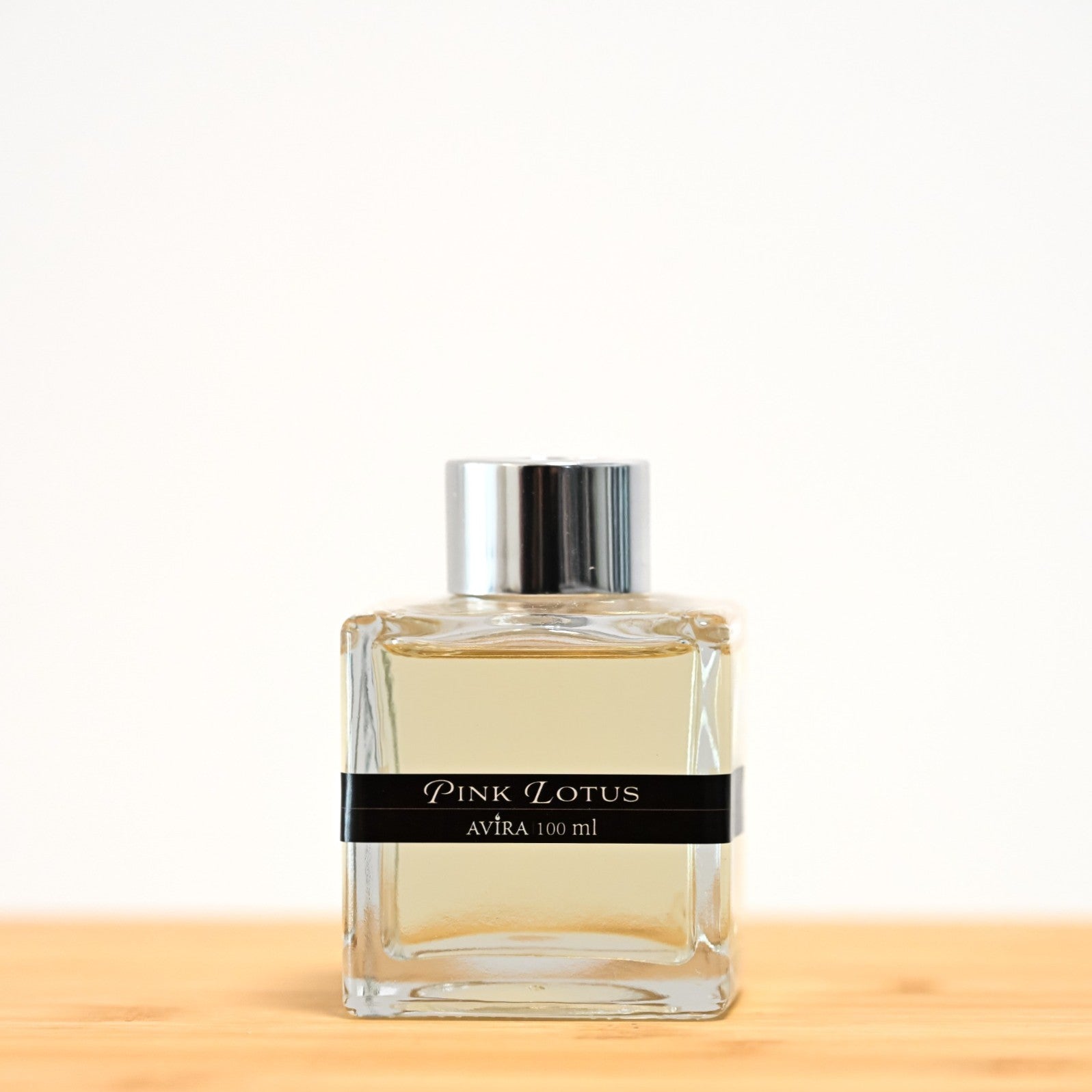 מפיץ ריח 100 מ"ל בניחוח לוטוס ורוד, בכלי זכוכית שקוף בצורת קובייה – אטום בפקק ומלווה בקולר כסוף – ובחזית מדבקת פס שחורה.