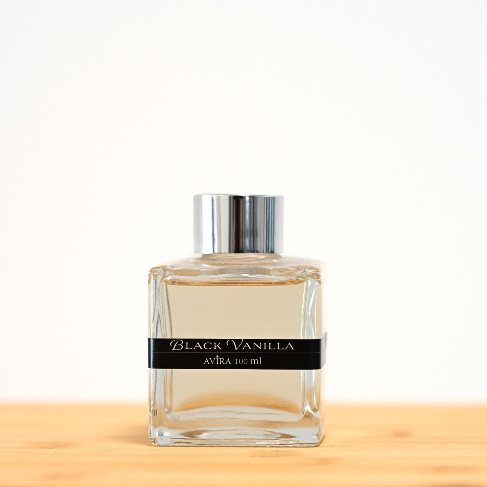 מפיץ ריח 100 מ"ל בניחוח בלאק ונילה, בכלי זכוכית שקוף בצורת קובייה – אטום בפקק ומלווה בקולר כסוף – ובחזית מדבקת פס שחורה.