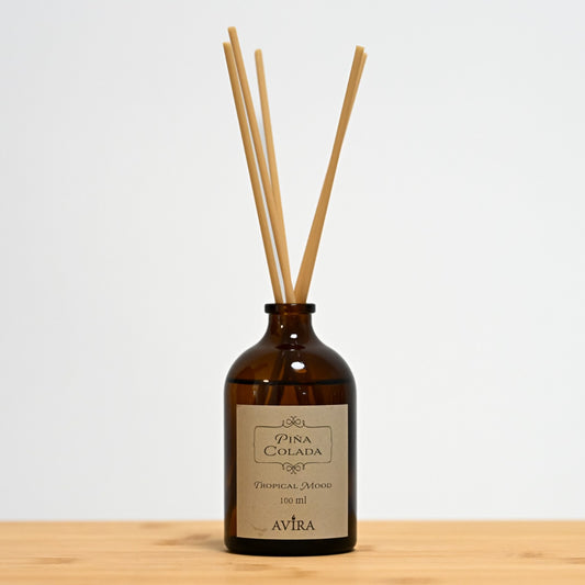 מפיץ ריח 100 מ"ל בניחוח פינה קולדה עם מקלות דמויי עץ, בכלי זכוכית חום ("בקבוק רוקחים") אטום בפקק שעם – ועליו מדבקה עם הכיתוב "TROPICAL MOOD".